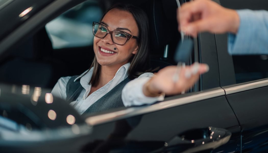 A woman, smiling broadly, leans forward from inside her car to reach for keys being handed over by another person, capturing a moment of joy and accomplishment in car acquisition.
Adonis Rent a Car